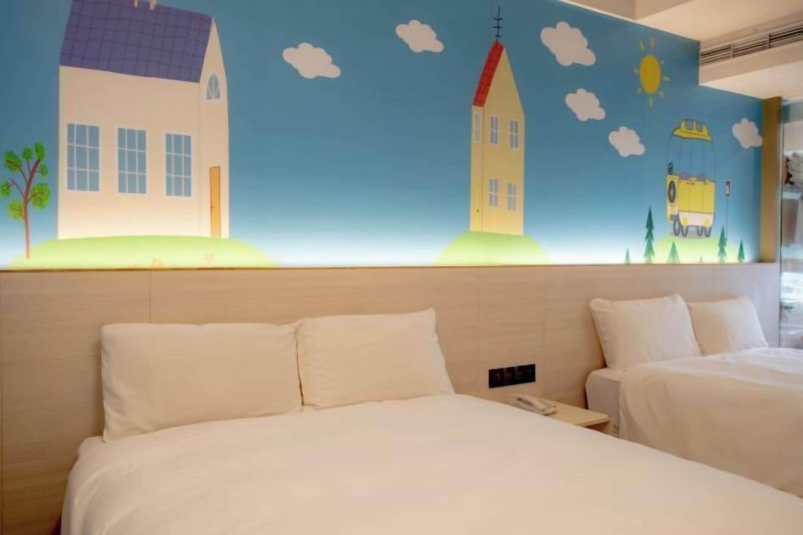Quarto de hotel com duas camas, um mural grande na parede retratando casas e um carro amarelo, e um design simples e limpo.