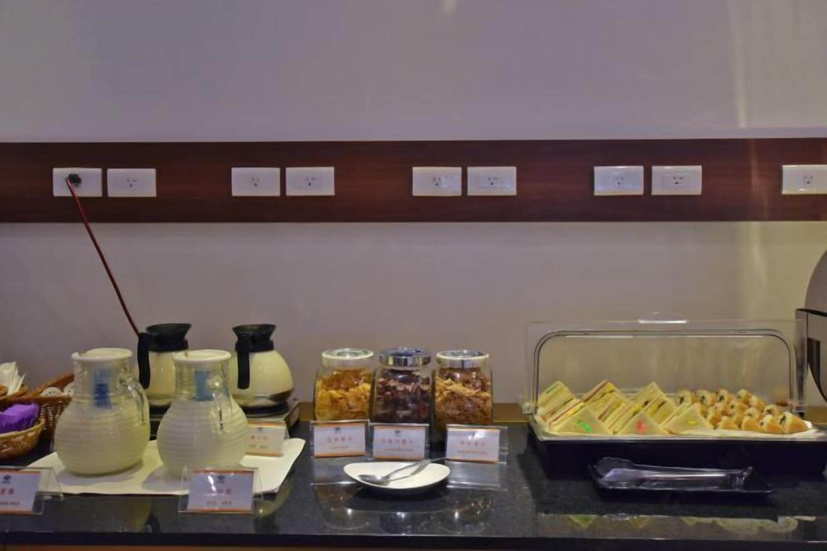 A buffet counter with various food items, including jars of pickled vegetables, a tray of sandwiches, and a pitcher of milk.