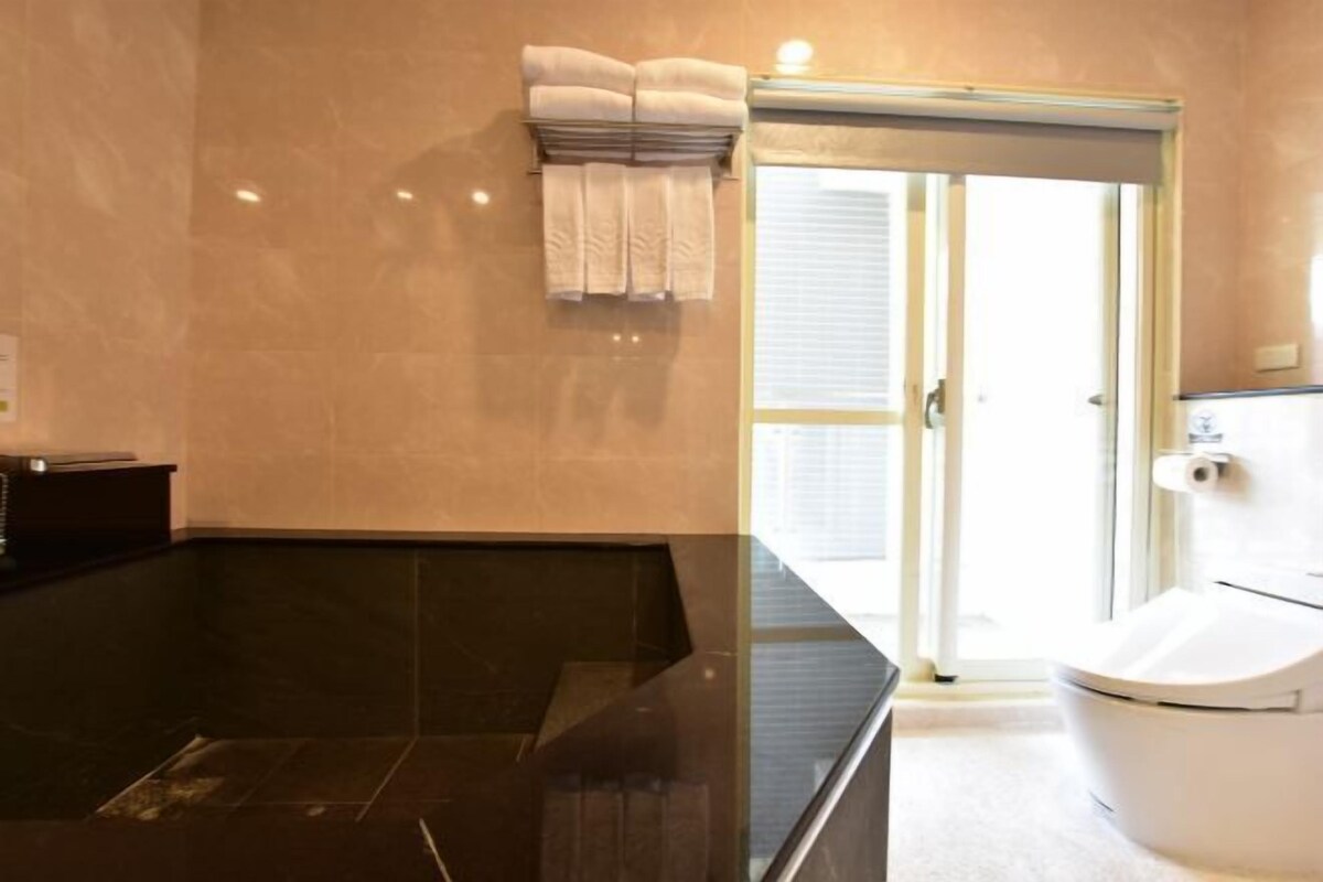 A modern bathroom with a black marble sink, a white toilet, and a glass shower door.