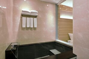 A modern bathroom with a black bathtub, a towel rack with folded towels, and a wooden panel wall. - Muen Yuan Dong Hot Spring Hotel (Yilan)