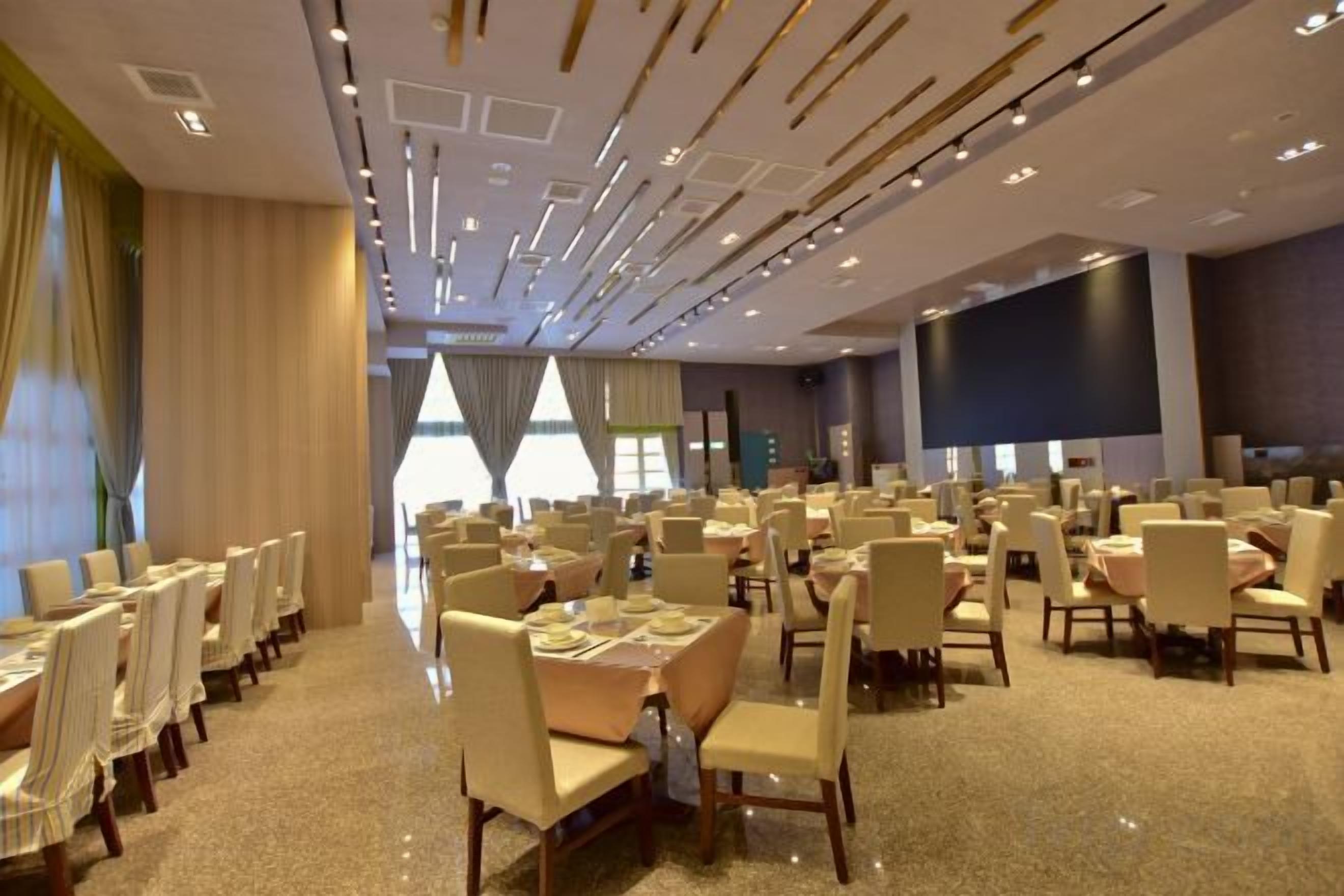 A spacious banquet hall with multiple tables and chairs, large windows, and a modern ceiling design.