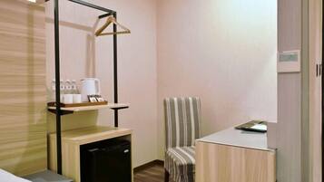 A compact hotel room with a kitchenette, a striped chair, a small table, and a hanging coat rack.