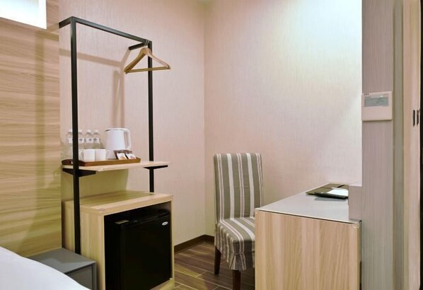 A compact hotel room with a kitchenette, a striped chair, a small table, and a hanging coat rack. - Muen Yuan Dong Hot Spring Hotel (Yilan)