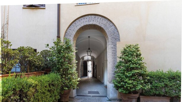 An arched entrance to a building with a cobblestone path leading through it, flanked by potted plants and a metal gate. - Quiet Trevi Fountain Apartment • Patio and Courtyard  (Roma)