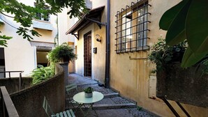 A narrow alleyway with a small table and chairs, a potted plant, and a door with a barred window. - Quiet Trevi Fountain Apartment • Patio and Courtyard  (Roma)