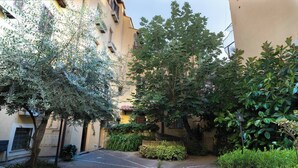 A courtyard with a paved path, trees, and a building with balconies. - Quiet Trevi Fountain Apartment • Patio and Courtyard  (Roma)