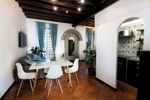 Cozy living space with a dining area, kitchen, and sofa, featuring a television and a white table with four chairs.