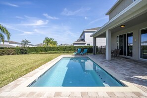 Una piscina con un borde de baldosas, un patio cubierto y vistas a casas vecinas.