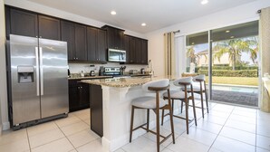 Una cocina moderna con refrigerador de acero inoxidable, gabinetes oscuros, microondas y una isla grande con taburetes de bar.