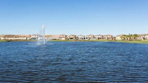 Un quartier résidentiel avec des maisons au bord d’un lac, une fontaine dans l’eau et un ciel dégagé.