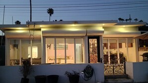A modern house with a covered porch, large windows, and a small garden area with potted plants. - BEACHFRONT NEWLY BUILT 3 BD 2 BA SURFPOINT SWEEPING OCEAN VIEW HOME! SW SWELLS! (Ensenada)