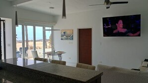 A modern living room with a large TV, a dining area, and a view of the outdoors. - BEACHFRONT NEWLY BUILT 3 BD 2 BA SURFPOINT SWEEPING OCEAN VIEW HOME! SW SWELLS! (Ensenada)