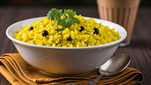 A bowl of yellow rice garnished with black beans and cilantro, accompanied by a glass of tea and a spoon on a wooden table. - Radhe Krishna Hotel and Restaurant (Nagaur)