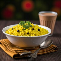 Un tazón de arroz amarillo adornado con frijoles negros y cilantro, acompañado de un vaso de té y una cuchara sobre una mesa de madera.