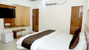 A bedroom with a bed, a TV, an air conditioner, a wooden door, and a small table. - Radhe Krishna Hotel and Restaurant (Nagaur)