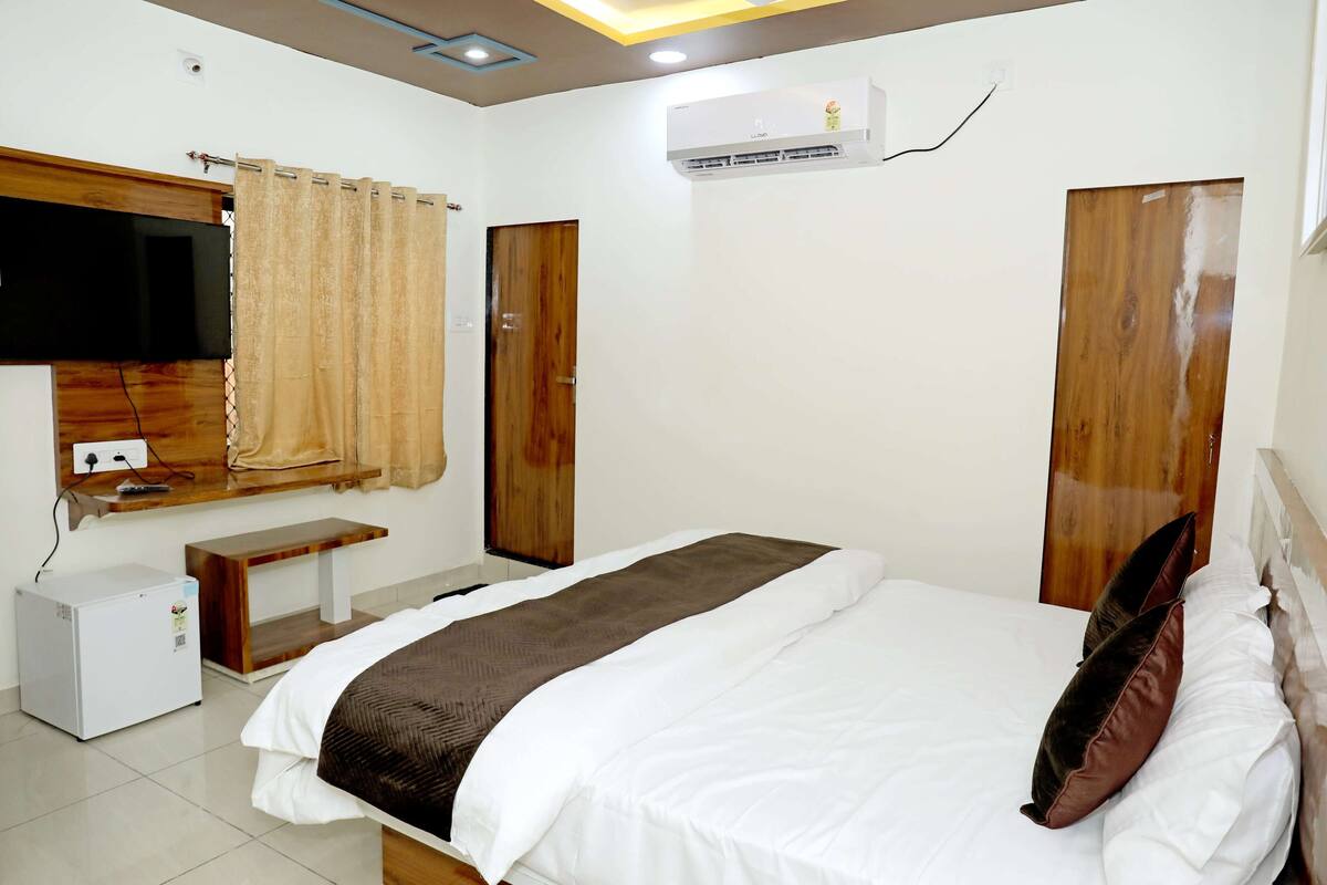 Une chambre à coucher avec un lit, une télévision, un climatiseur, une porte en bois et une petite table.