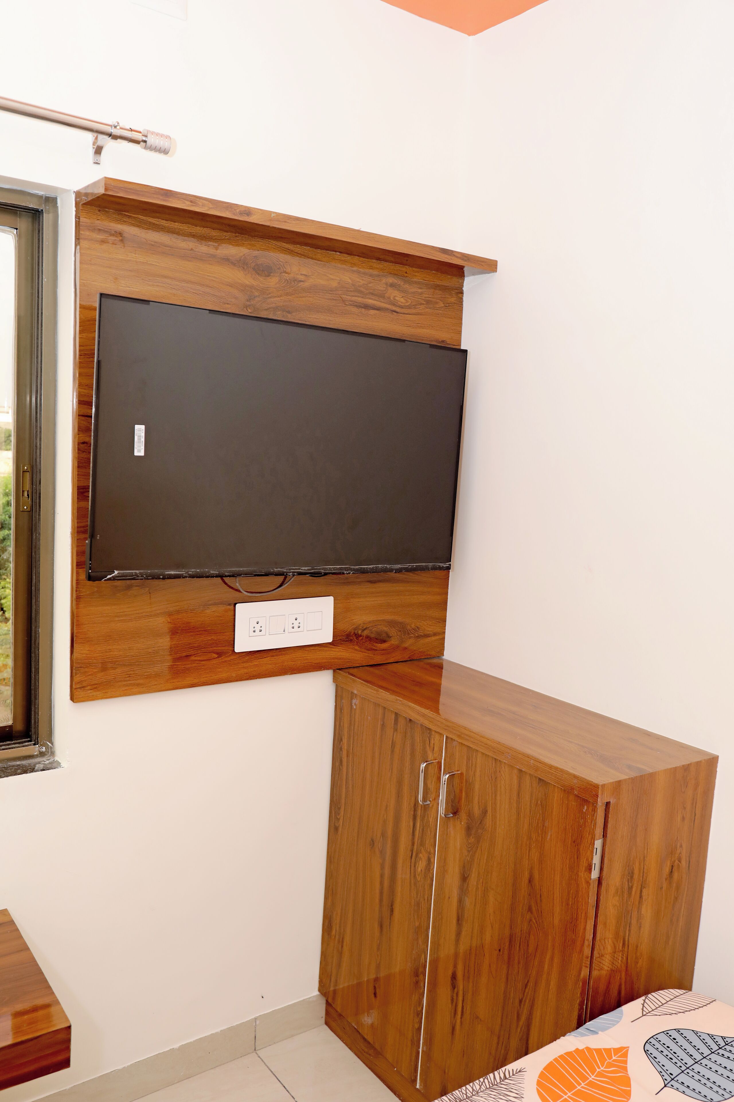 A room with a mounted TV on a wooden panel, a wooden cabinet below it, and a power outlet on the wall.