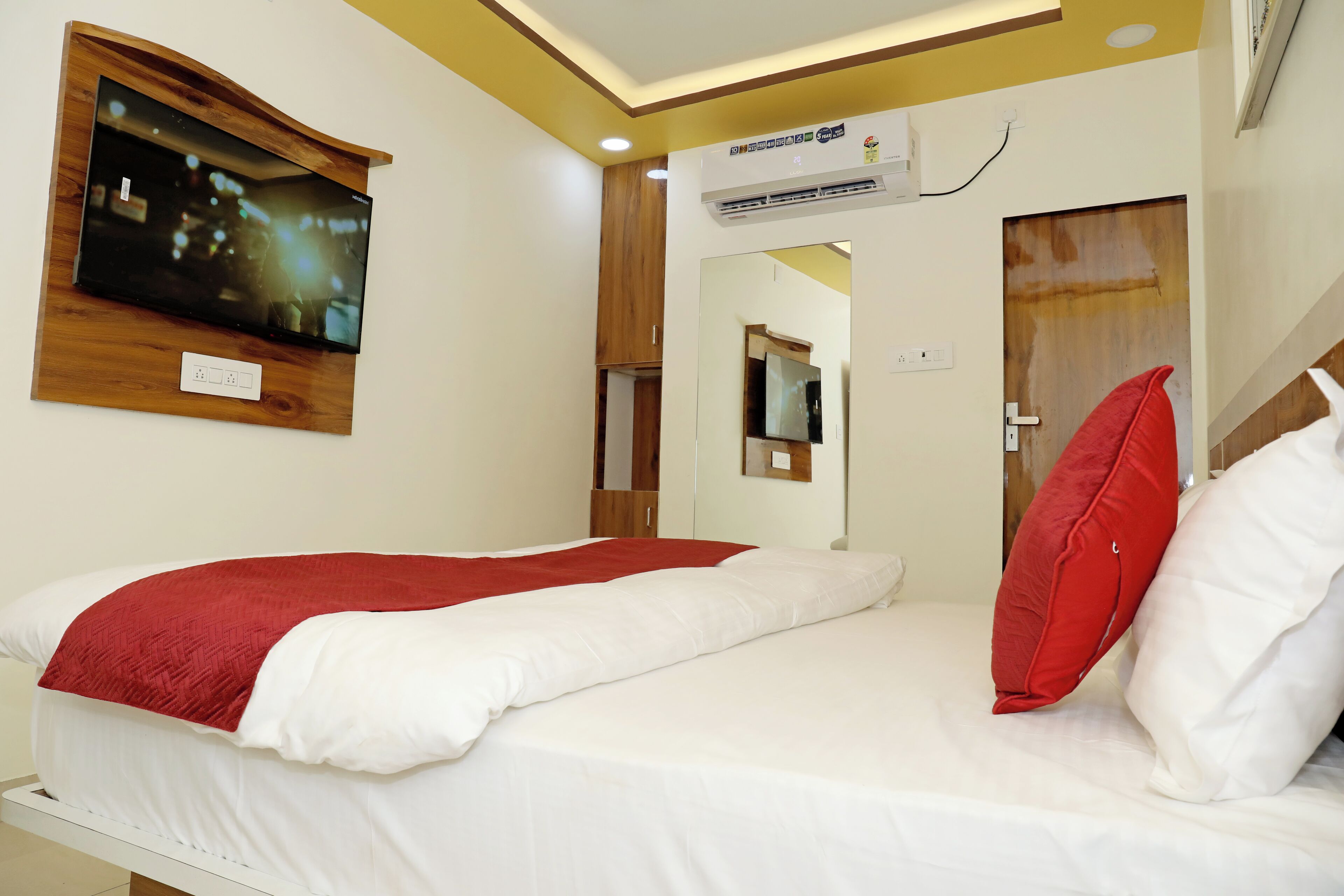 A hotel room with a bed, a TV mounted on the wall, an air conditioning unit, and a mirror.