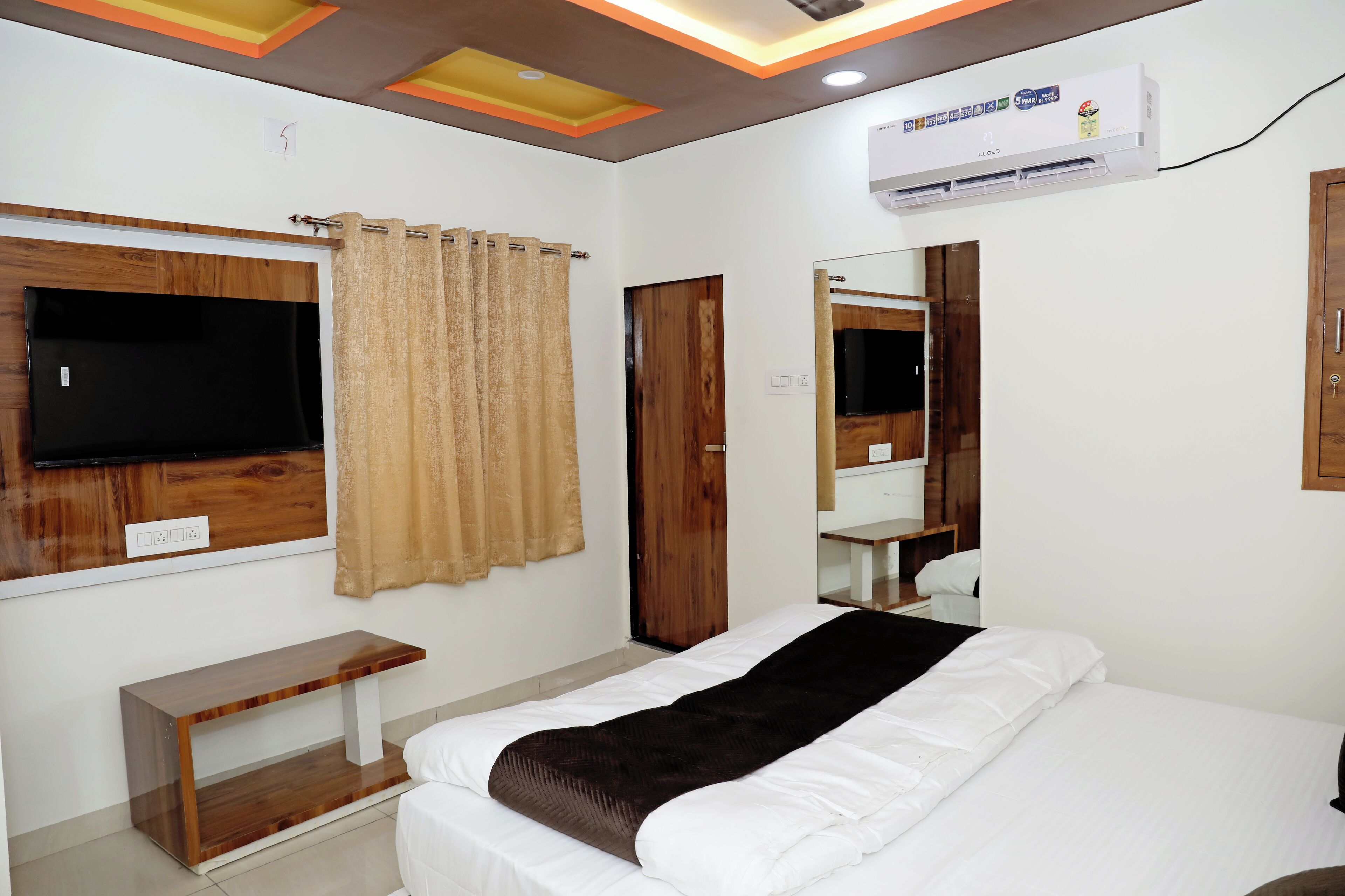 Habitación de hotel con una cama, televisión montada en la pared, un banco de madera, un espejo y un equipo de aire acondicionado.