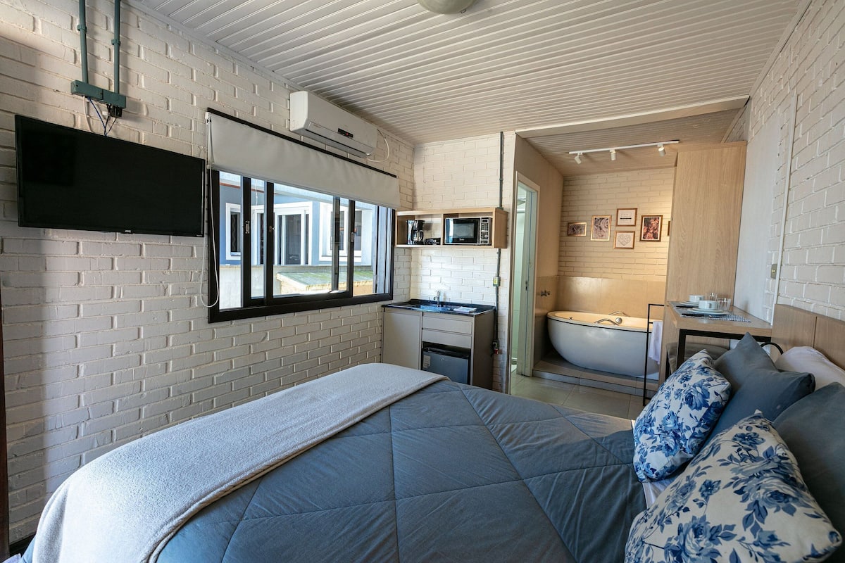 A modern hotel room with a bed, a flat-screen TV, a kitchenette, and a bathroom.