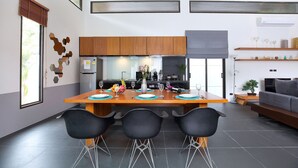 A modern kitchen with wooden cabinets, a dining table set for four, and a grey sofa in the living area. - Elegant 3BR Pool Villa Coco B6 in Kamala (Kamala)