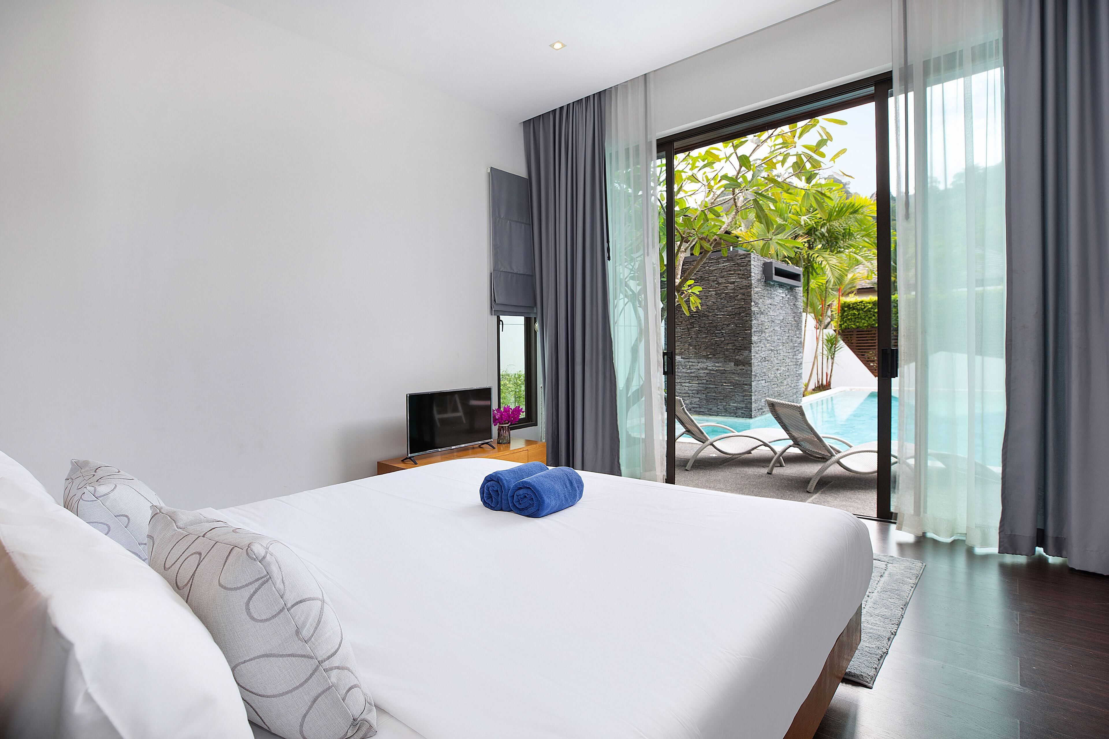 Ein modernes Hotelzimmer mit einem großen Bett, einem Fernseher und Blick auf einen Außenpool.