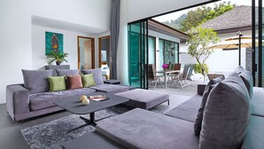 A modern living room with a grey sofa, a coffee table, and a dining area with chairs and a table. - Elegant 3BR Pool Villa Coco B6 in Kamala (Kamala)