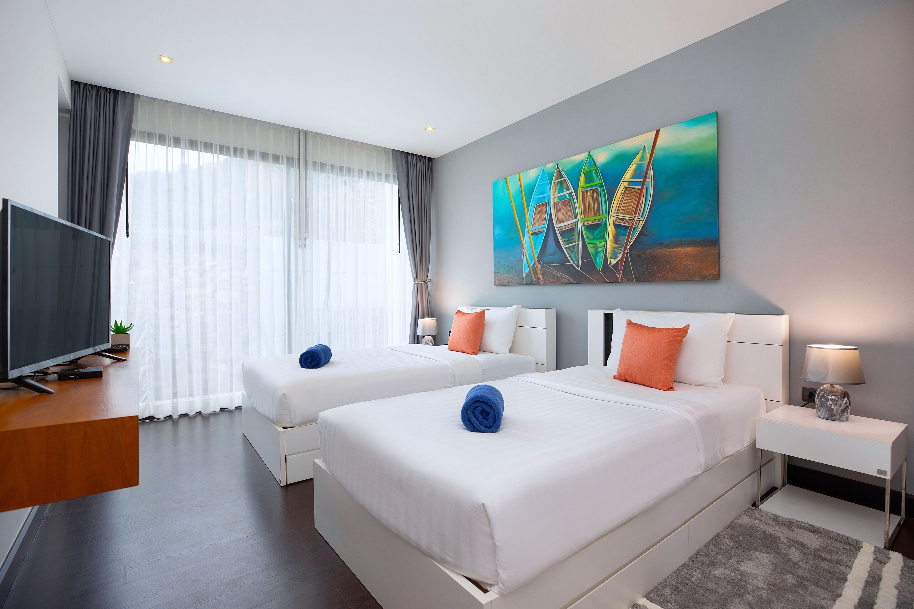 A hotel room with two beds, a TV, and a painting of boats.