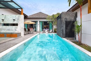 Ein moderner Poolbereich mit klarem, blauem Wasser, Liegestühlen und einer verglasten Terrasse.