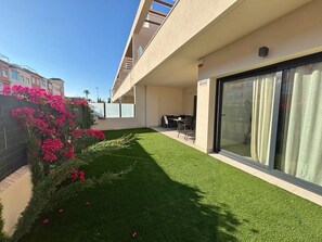 A modern building with a flat roof, a glass door, and a small patio area with artificial grass and a table.