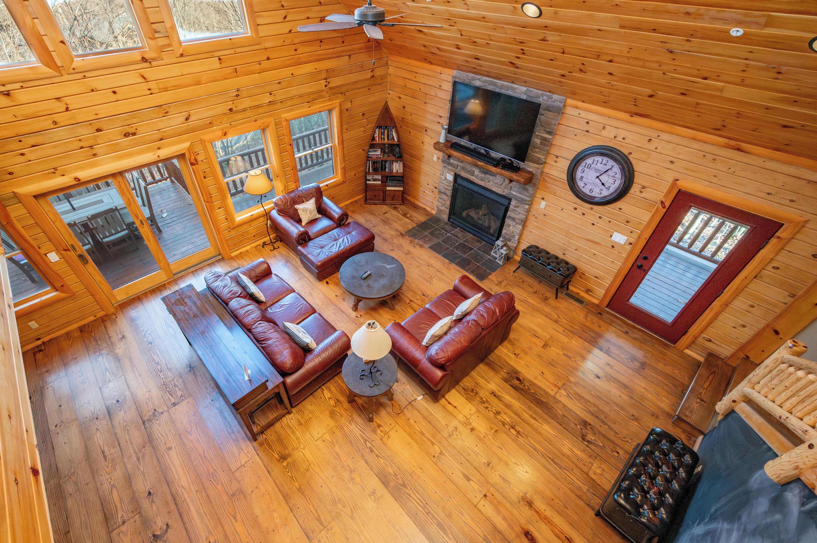 A log cabin interior with a living room, fireplace, television, and a clock on the wall.
