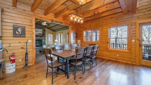 A wooden cabin interior with a dining table, chairs, a fireplace, and large windows. - Dog Friendly Mountain Retreat w/ Bar & Hot Tub (McHenry)