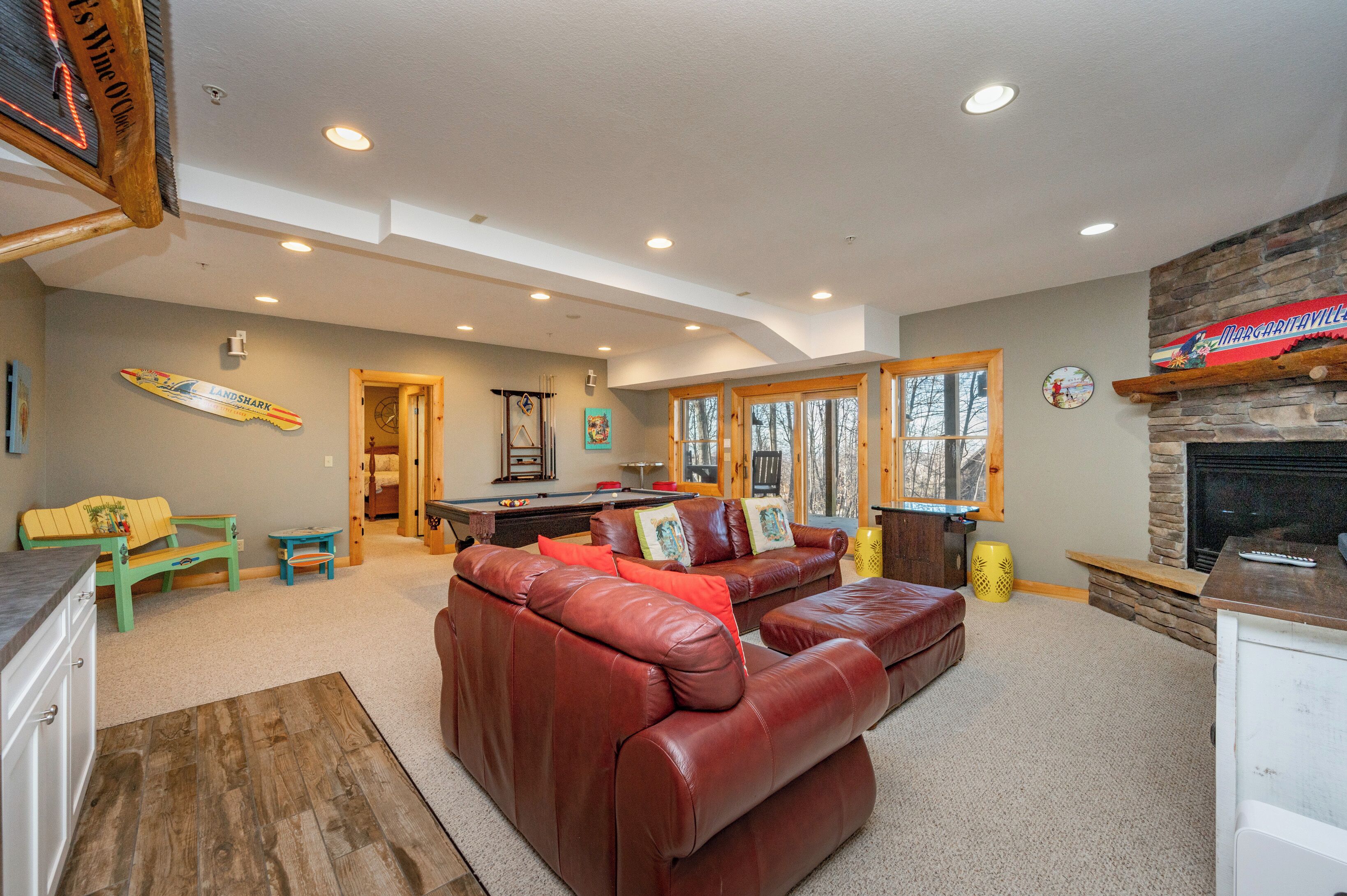 A spacious living room with a leather sofa, a pool table, and a stone fireplace.