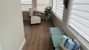 A room with a wooden ceiling, a bench with a basket of towels, a chair with a cushion, and a table with a plant. - Charming Farmhouse on 2 acres, Sleeps 8. Only 5 mins from Richards Point beach (Borden-Carleton)