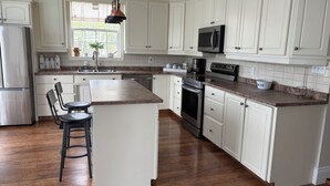 A kitchen with white cabinets, a central island, stainless steel appliances, and a window with a view. - Charming Farmhouse on 2 acres, Sleeps 8. Only 5 mins from Richards Point beach (Borden-Carleton)