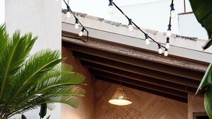 A reception area with a herringbone-patterned floor, a hanging light fixture, a 'hola' sign, and two white barstools.