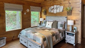 A cozy wooden cabin bedroom with a large bed, two bedside tables, and a window with a view of greenery. -  Eureka Springs Riverview Oasis: A Serene Retreat Overlooking the White River  (Eureka Springs)