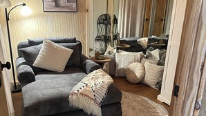 A cozy living room with a sectional sofa, a small round table, and a decorative mirror. -  Eureka Springs Riverview Oasis: A Serene Retreat Overlooking the White River  (Eureka Springs)