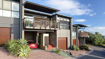A modern two-story house with a balcony, a garage, and a red car parked in front.