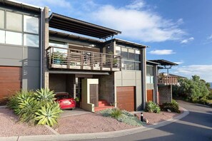 A modern two-story house with a balcony, a garage, and a red car parked in front.