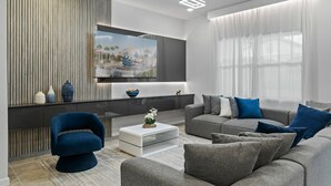 Ein modernes Wohnzimmer mit Flachbildfernseher, grauen Sofas, einem blauen Sessel und einer dekorativen Vase auf einem Konsolentisch.
