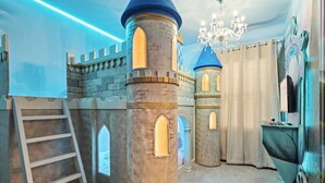 Ein kindgerechtes Spielzimmer im Burgstil mit einer Leiter, einem Turm und einer Chandelier.