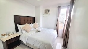 Habitació d'hotel amb un llit, una tauleta de nit, una finestra amb cortines i un aparell d'aire condicionat a la paret.