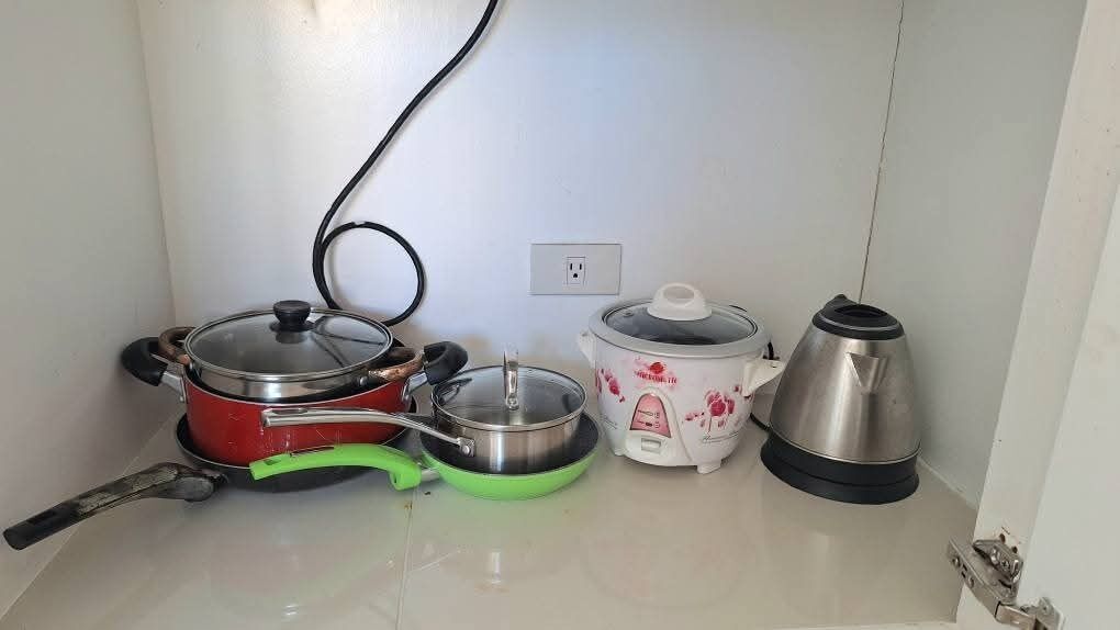 Una encimera de cocina con una olla roja, una sartén verde, una olla de cocción lenta blanca y un hervidor eléctrico plateado.