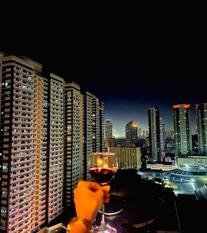 A high-rise building with multiple floors and a glass facade, viewed from a balcony at night. - Yhen Airbnb Manila (Manila)