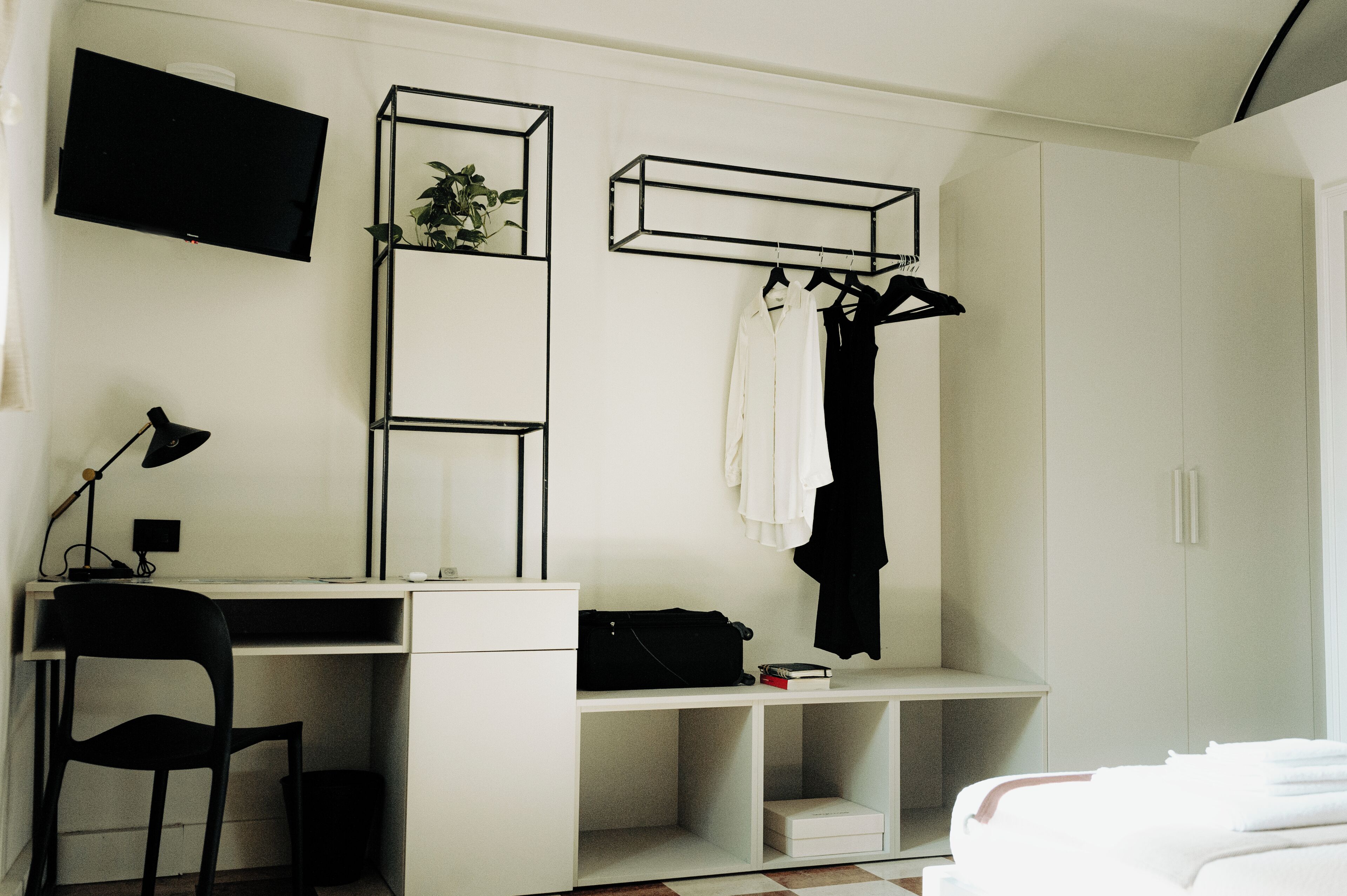 A bedroom with a bed, a desk with a chair, a TV, and a wardrobe.