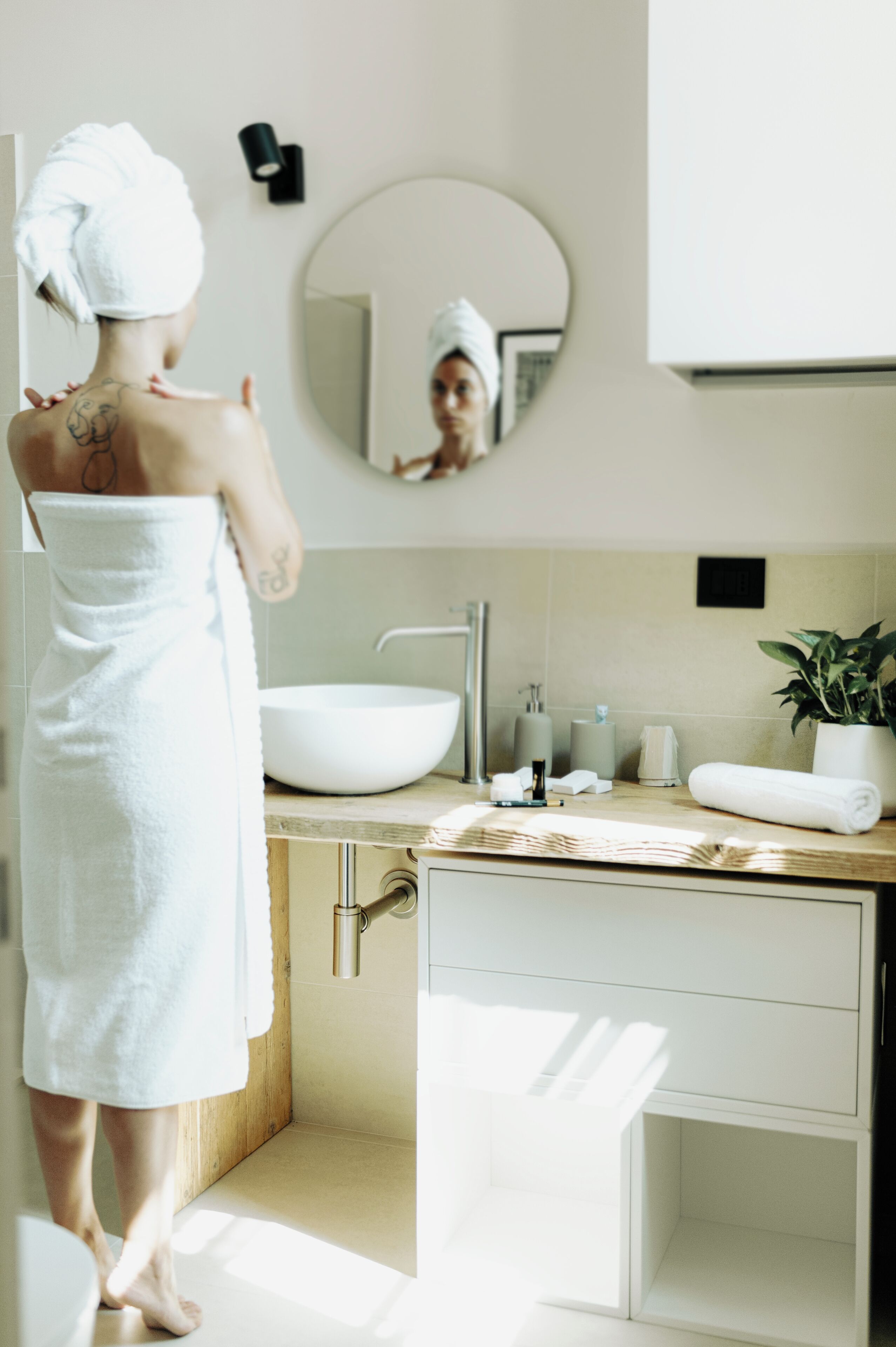 A modern bathroom with a large mirror, a white sink, and a potted plant.