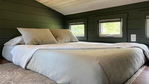 A bedroom with a large bed, two windows with blinds, a wooden ceiling, and a green wall. - Sagebrush Caboose (Oliver)