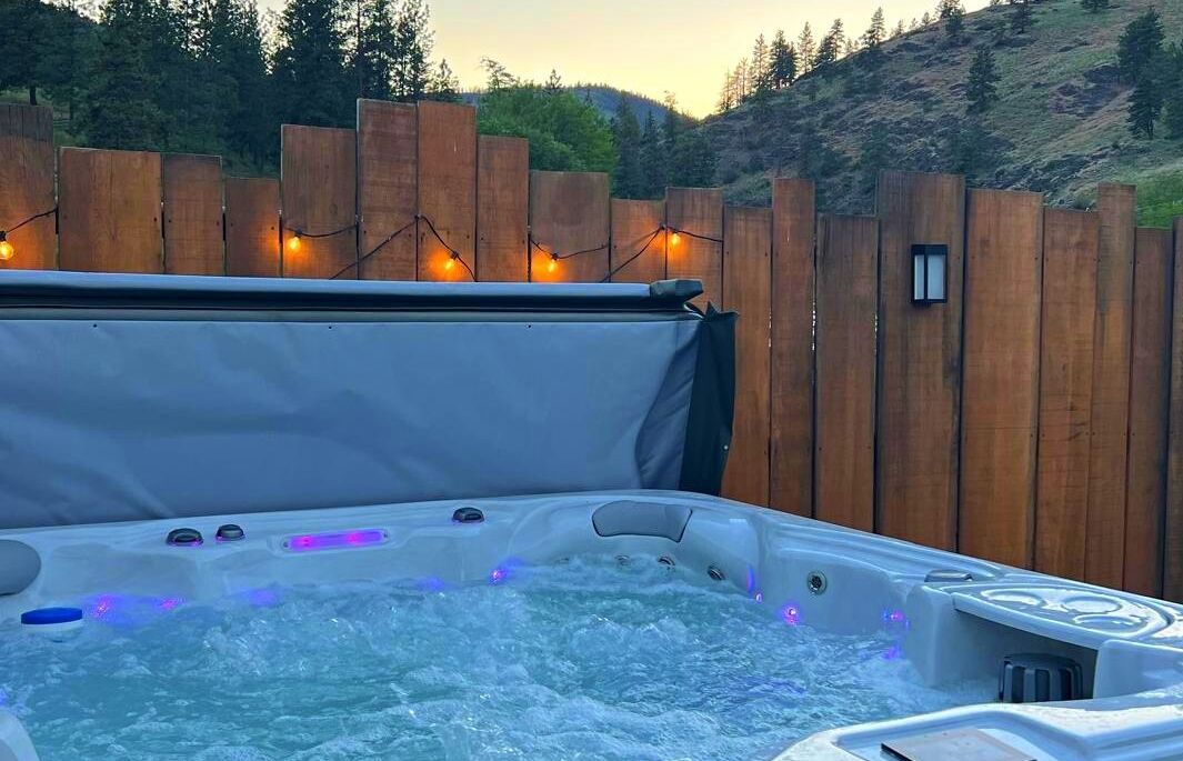A hot tub with a wooden fence and string lights in the background.
