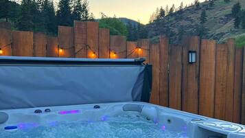 A hot tub with a wooden fence and string lights in the background.